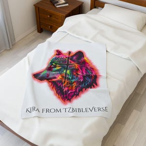 Op de afbeelding: Een witte deken met een kleurrijk wolfskopontwerp en de tekst "Kira from TZBIBLEVERSE".