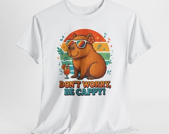 May include: White t-shirt featuring a cartoon capybara wearing sunglasses and a flower, with a cocktail and musical notes. The text "DON'T WORRY, BE CAPPY!" is printed below the illustration. The design has a retro sunset background.
