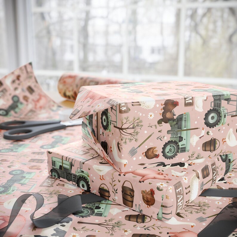 May include: Two wrapped gift boxes with pink farm-themed wrapping paper. The paper features illustrations of tractors, farm animals, and tools. Scissors and a roll of matching paper are visible, along with a grey ribbon.