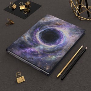 May include: A purple and blue notebook with a black hole and galaxy design. The notebook is lying on a gray surface with two pencils next to it.