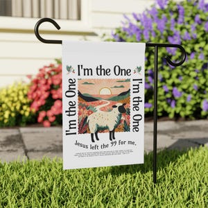 以下が含まれることがあります： 「I'm the One」の文字と、夕焼けの中の羊のグラフィックが描かれた白いガーデンフラッグ。フラッグには「Jesus left the 99 for me.」の文字も含まれています。