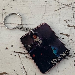 May include: A white ceramic mug with a black handle and the text "But First, Coffee" in a bold, black font. The mug is set against a blurred background, suggesting a cozy setting. The mug appears to be approximately 4 inches tall.