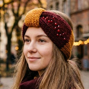 Puede incluir: Una diadema de punto grueso con una base de color burdeos intenso y un detalle central anudado en amarillo mostaza. La sección burdeos está adornada con pequeñas cuentas rojas dispersas. El accesorio está hecho de lana gruesa acanalada.