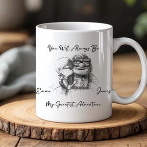 May include: White ceramic mug featuring a black and white illustration of a couple with the text "You Will Always Be" and "My Greatest Adventure". Names "Emma" and "James" are also included. The mug sits on a wooden coaster.