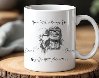 May include: White ceramic mug featuring a black and white illustration of a couple with the text "You Will Always Be" and "My Greatest Adventure". Names "Emma" and "James" are also included. The mug sits on a wooden coaster.