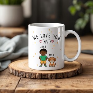 Może przedstawiać: Biały ceramiczny kubek z czarnym napisem WE LOVE YOU DAD i dwoma czerwonymi sercami. Poniżej znajduje się ilustracja przedstawiająca dziecko o imieniu JACK w zielonej koszulce i żółtych spodenkach obok brązowego psa o imieniu MAX, wśród złotych gwiazdek.