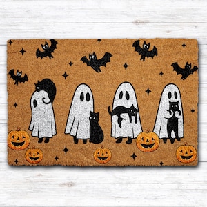 May include: A rectangular doormat with a Halloween theme. The mat features four white ghosts, black cats, bats, and jack-o'-lanterns on a brown background. The design includes black stars and is suitable for seasonal home decor.