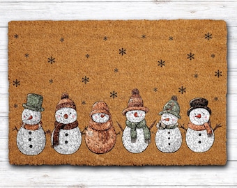 May include: A rectangular doormat with a brown background and a row of six snowmen. Each snowman has a different hat and scarf. Black snowflakes are scattered across the top of the mat. The doormat is made of a textured material.