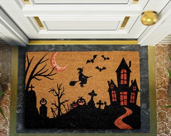 Puede incluir: Felpudo de Halloween con una escena espeluznante. El diseño incluye una silueta de una casa embrujada, una bruja en una escoba, murciélagos, calabazas, una luna creciente y lápidas. Hecho de fibra natural.