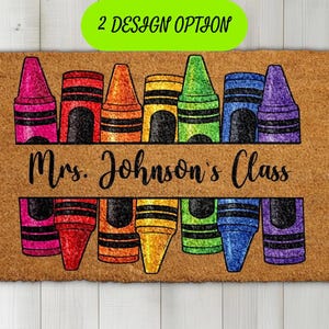 May include: A rectangular tan coir doormat featuring a colorful graphic of crayons in pink, red, orange, yellow, green, blue, and purple. The text "Mrs. Johnson's Class" is printed in black script across the center of the crayon design.