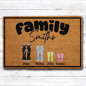 May include: A rectangular doormat with the word "Family" in large, black, bold letters above the family name "Smiths" in cursive. Below are illustrations of boots in black, light blue, green, and pink, with names below each.