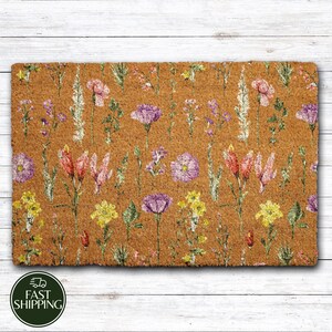 May include: A rectangular doormat with a brown background and a repeating floral pattern. The flowers are in shades of pink, purple, and yellow, with green stems and leaves. The doormat is made of a natural fiber material.
