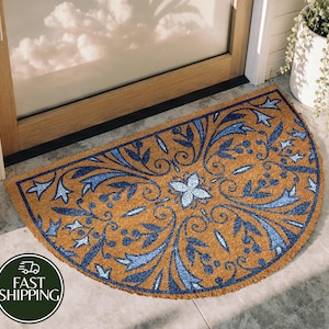 May include: A half-circle doormat with a brown background and a blue floral design. The mat is made of a natural fiber material and is placed in front of a wooden door. The words "Fast Shipping" are in a green circle.