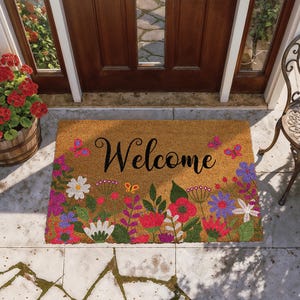 May include: A rectangular doormat with the word "Welcome" in black script. The mat is tan with a colorful floral border featuring red, pink, purple, and white flowers, and butterflies.