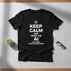 May include: Black t-shirt featuring the white text "KEEP CALM AND TRUST THE AI", with the additional text "JUST KIDDING ALWAYS DOUBLE-CHECK". A small potted plant and spectacles are also visible.