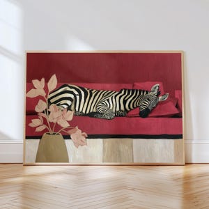 May include: A framed artwork depicts a zebra resting on a red sofa. The zebra has black and white stripes. A gold vase with pink flowers is on the left. The artwork is in a light wood frame.
