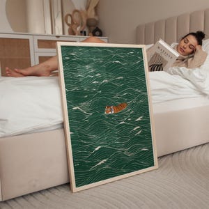 Pu&ograve; includere: Una stampa artistica incorniciata con una tigre che nuota in un mare di onde verdi. L'opera d'arte ha uno stile minimalista con linee di onde bianche. La tigre &egrave; arancione e nera. La cornice &egrave; di colore legno chiaro.