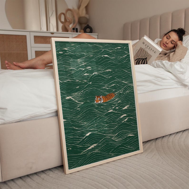 Pu&ograve; includere: Una stampa artistica incorniciata con una tigre che nuota in un mare di onde verdi. L'opera d'arte ha uno stile minimalista con linee di onde bianche. La tigre &egrave; arancione e nera. La cornice &egrave; di colore legno chiaro.