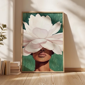 May include: A framed art print featuring a woman's face partially obscured by a large, white flower. The artwork has a green background and a wooden frame. The woman's skin is a warm brown tone, and her lips are a soft pink.