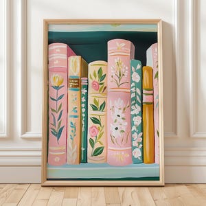 May include: A framed art print featuring a collection of stylized books. The books are painted in pastel pink, green, and yellow, adorned with floral and botanical designs. The artwork is set against a teal background, creating a decorative and artistic display.