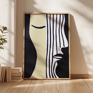 May include: Abstract art print featuring a minimalist face design. The artwork is divided into sections of black, cream, and white vertical stripes. The framed print is displayed on a wooden floor.