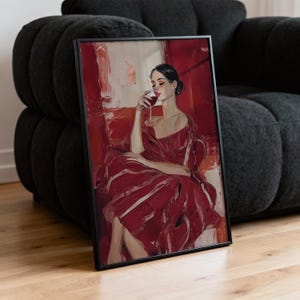Op de afbeelding: Ingelijste kunstdruk met een vrouw in een rode jurk die geniet van een glas rode wijn. Het kunstwerk heeft een schilderkunstige stijl met een rood en wit kleurenpalet. De print zit in een zwart frame.