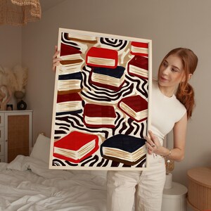 May include: A framed art print featuring an abstract design of books in red, navy, and brown. The books are set against a beige and black zebra-striped background. The frame is a light wood color.