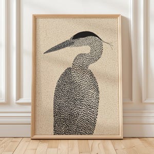 May include: A framed art print featuring a stylized illustration of a heron. The heron is depicted in black and white, with a speckled body and a long, pointed beak. The background is a light beige with a dotted pattern.