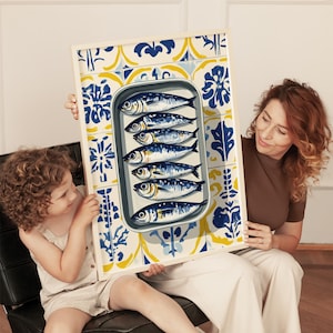 May include: A framed print featuring a tin of sardines. The sardines are arranged in a metal tin, set against a backdrop of blue, yellow, and white patterned tiles. The print is held by a woman and a child.