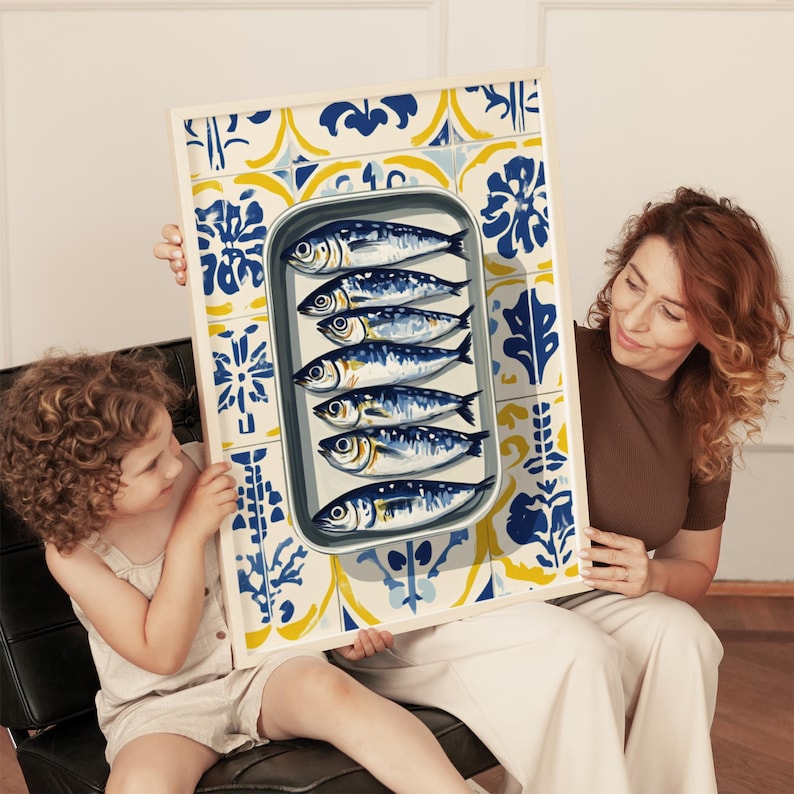 May include: A framed print featuring a tin of sardines. The sardines are arranged in a metal tin, set against a backdrop of blue, yellow, and white patterned tiles. The print is held by a woman and a child.