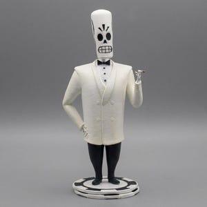 Puede incluir: Una figura estilizada de un personaje esquelético con cabeza alargada, que viste una chaqueta de esmoquin blanca de doble botonadura, pajarita negra y pantalones negros. La figura se apoya sobre una base circular que imita una ficha de póquer.