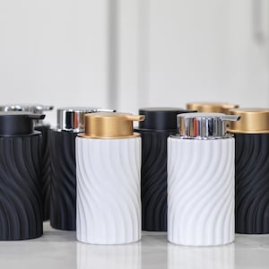 Pode incluir: Conjunto de seis dispensadores de sabonete de cerâmica preta e branca com designs ondulados. Os dispensadores têm bombas douradas e prateadas.