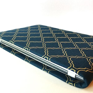 Könnte beinhalten: Eine tealblaue Laptoptasche mit einem goldenen geometrischen Muster. Die Tasche ist über einen Laptop gefaltet.