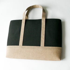 May include: A rectangular tote bag with a black upper section and a tan lower section. The bag has two tan handles and is made of a textured fabric. The bag is designed for carrying items.