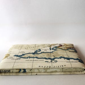 May include: A cream-colored fabric wallet with a vintage world map design. The map features blue oceans, brown landmasses, and black text. The wallet is folded closed and the text "ARCTIC OCEAN" is visible on the front.