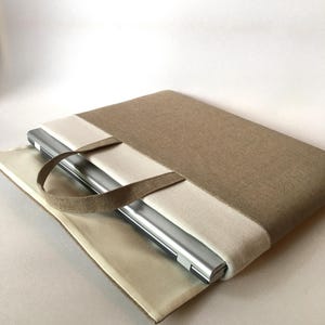 May include: A beige and cream laptop sleeve with a handle. The sleeve is made of a fabric material and has a zipper closure. A laptop is inside the sleeve.