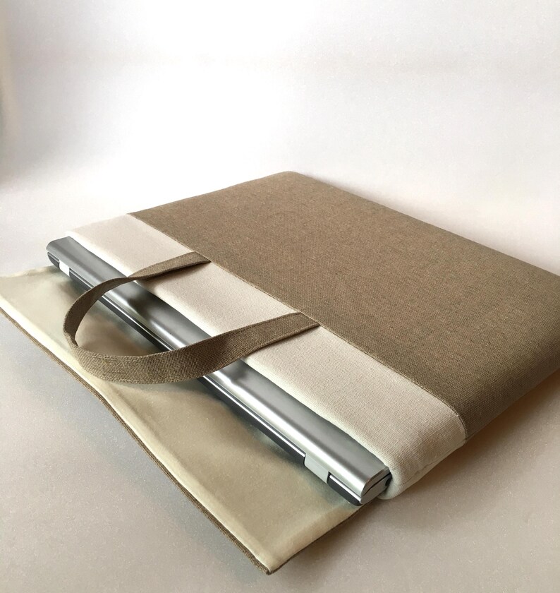May include: A beige and cream laptop sleeve with a handle. The sleeve is made of a fabric material and has a zipper closure. A laptop is inside the sleeve.