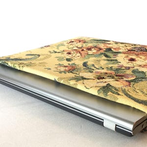 May include: A silver laptop partially inserted into a floral patterned laptop sleeve. The sleeve features a yellow background with a repeating pattern of flowers in shades of pink, green, and brown.