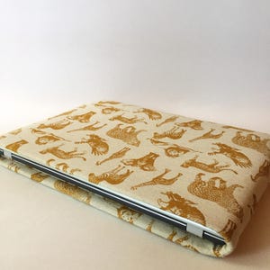 May include: A laptop sleeve with a beige linen fabric exterior and a gold print of various animals, including zebras, giraffes, and elephants.