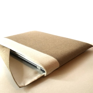 Könnte beinhalten: Eine braune und beige Laptop-Hülle mit einem Klappverschluss. Die Hülle ist aus einem weichen, strukturierten Stoff.