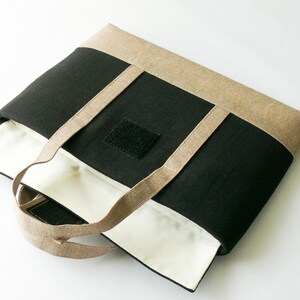 May include: A rectangular tote bag with a black center panel, tan top and bottom panels, and tan handles. The interior is white. A black square with velcro is on the front. The bag is open, revealing the white interior.