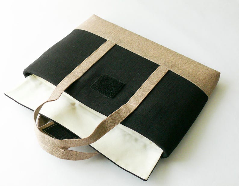 May include: A rectangular tote bag with a black center panel, tan top and bottom panels, and tan handles. The interior is white. A black square with velcro is on the front. The bag is open, revealing the white interior.