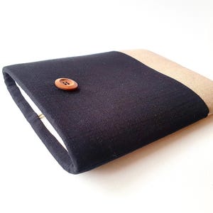 May include: A black and beige fabric laptop sleeve with a wooden button closure.