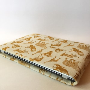 May include: A laptop sleeve with a beige linen fabric exterior and a gold print of various animals, including zebras, giraffes, and elephants.