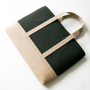 May include: A black and tan tote bag with a rectangular design. The bag features a black center panel and tan-colored top and bottom sections. Tan straps extend from the top of the bag for carrying.