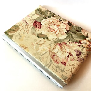 Könnte beinhalten: Eine Laptop-Hülle mit einem Blumenmuster. Der Stoff hat einen beigefarbenen Hintergrund mit großen weißen, rosa und roten Blumen, grünen Blättern und kleinen lila Blüten.