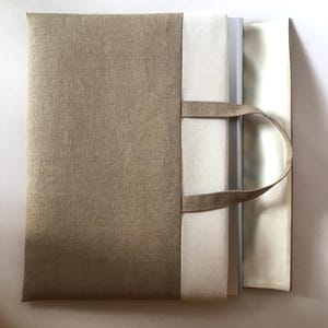 May include: A beige linen tote bag with a white lining and two handles. The bag is open and a stack of books is inside.