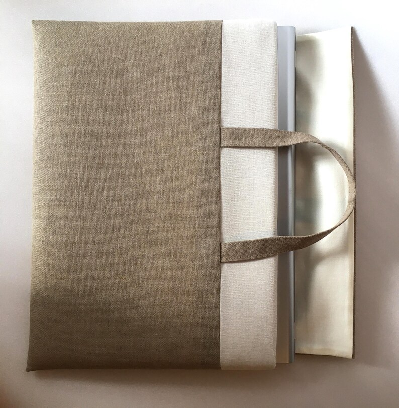 May include: A beige linen tote bag with a white lining and two handles. The bag is open and a stack of books is inside.