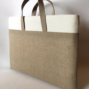 May include: A brown and white tote bag with two fabric handles. The bag is made of a natural fabric with a textured weave.