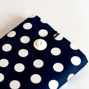 May include: A navy blue fabric pouch with white polka dots and a white button closure. The pouch is made of a soft, durable fabric and is perfect for storing small items.